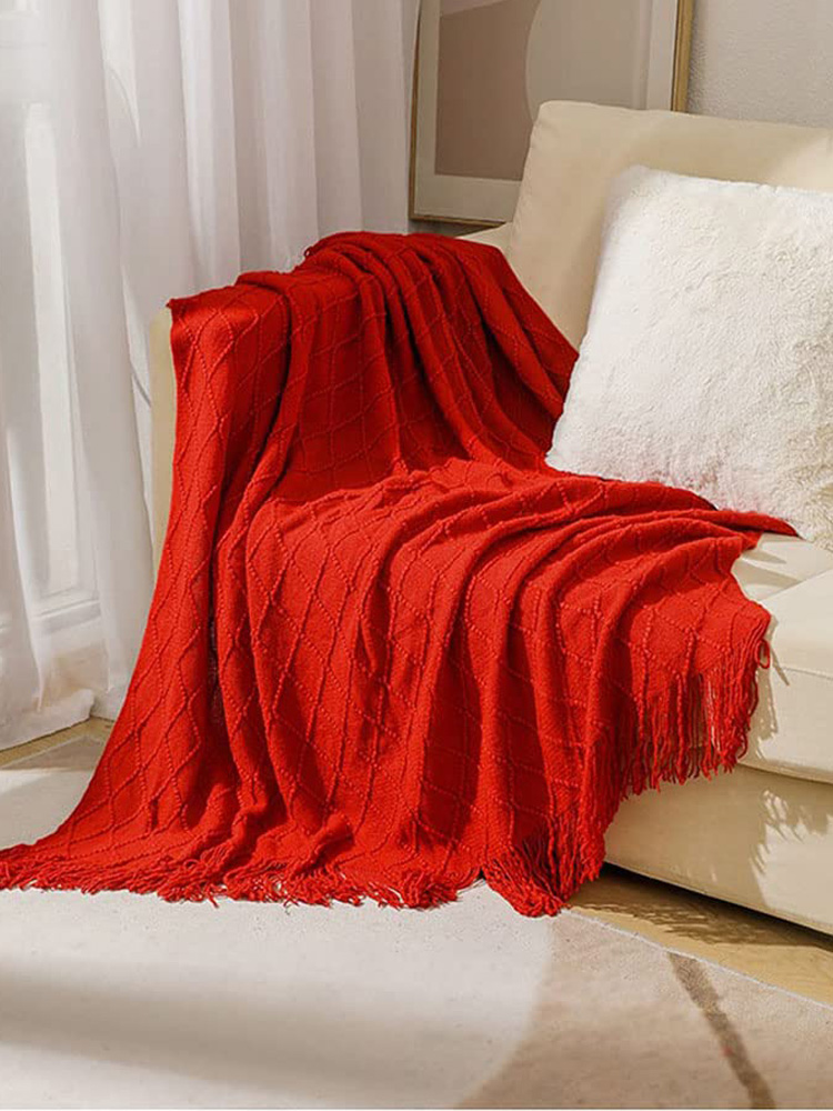 Vibrant red knitted tassel throw blanket draped over light sofa, cozy home decor for self care relaxation