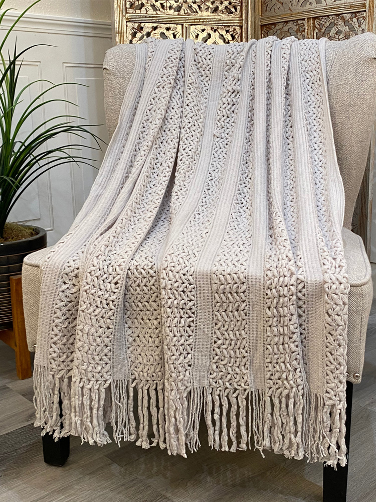 White hollow knit tassel throw blanket draped over armchair, minimalist cozy home decor for self care relaxation