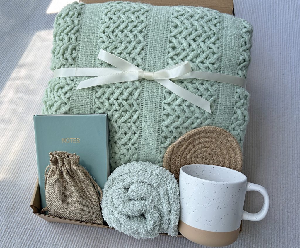 Nestlygift sage green self care gift set with knit blanket, ceramic mug, fuzzy socks, journal and scented sachet