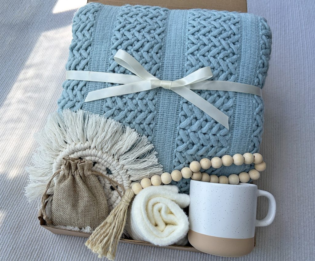 Nestlygift light blue self care gift set with fringed knit blanket, ceramic mug, fuzzy socks and linen scented sachet, neutral flat lay