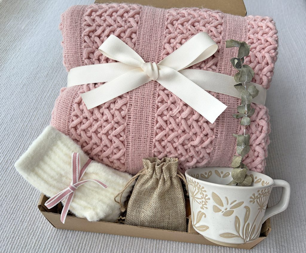 Nestlygift blush pink self care gift set with knitted throw blanket, floral ceramic mug, fuzzy socks, scented pouch and dried eucalyptus