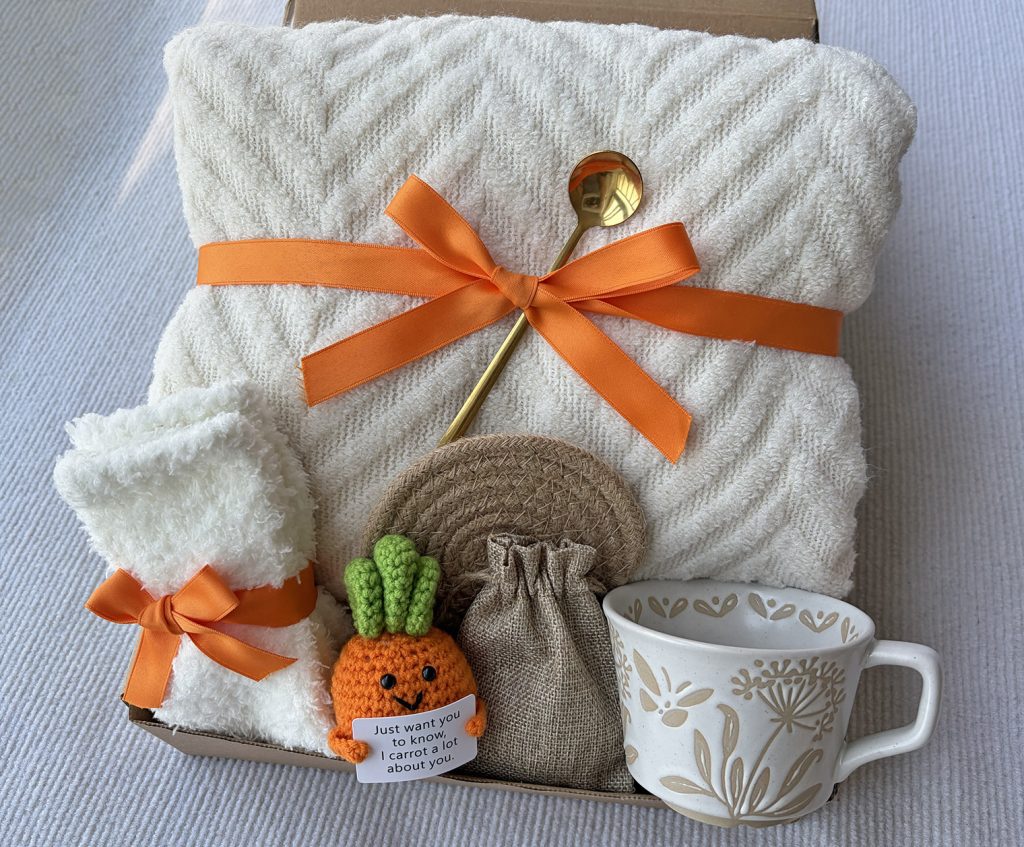 Nestlygift cream self care gift box with wavy knit blanket, cute crochet carrot ornament, floral ceramic mug and fluffy socks